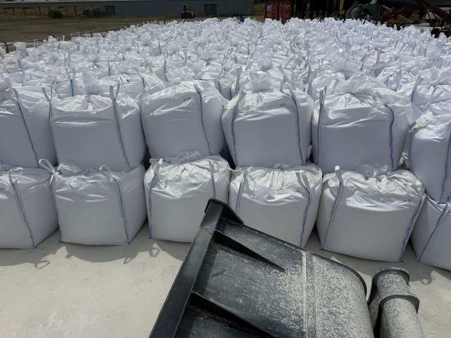 Filled white bulk bags stacked two high, with the forks of a loader in the foreground