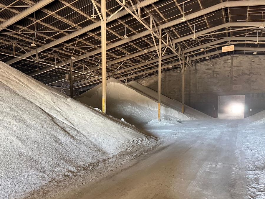 A large bank of granular material inside a steel-framed storage building, with a lit doorway at the far end