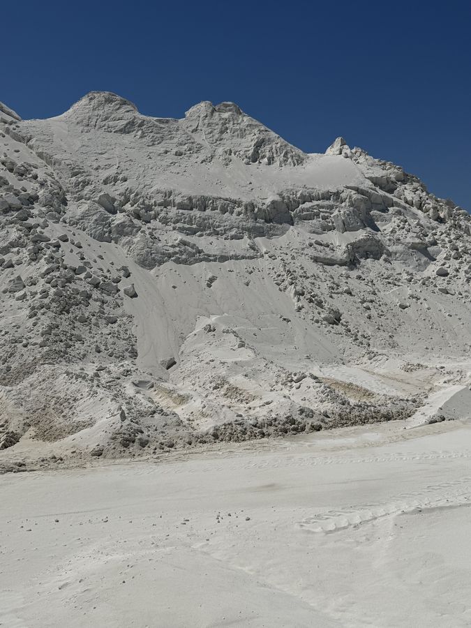 Close view of a white aragonite stockpile face, with weathered ledges and loose grain below