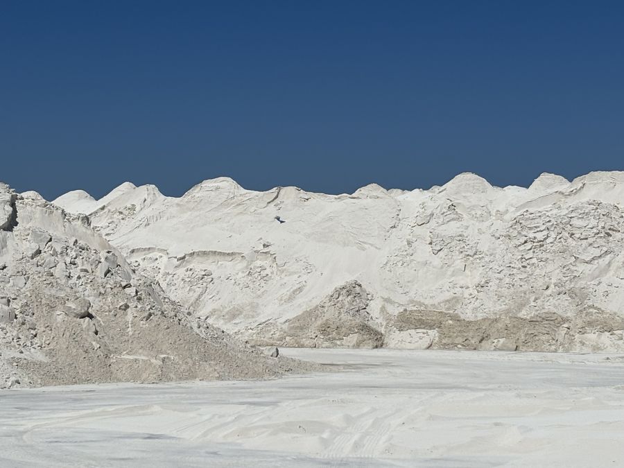 A long ridge of white aragonite stockpiles against a deep blue sky
